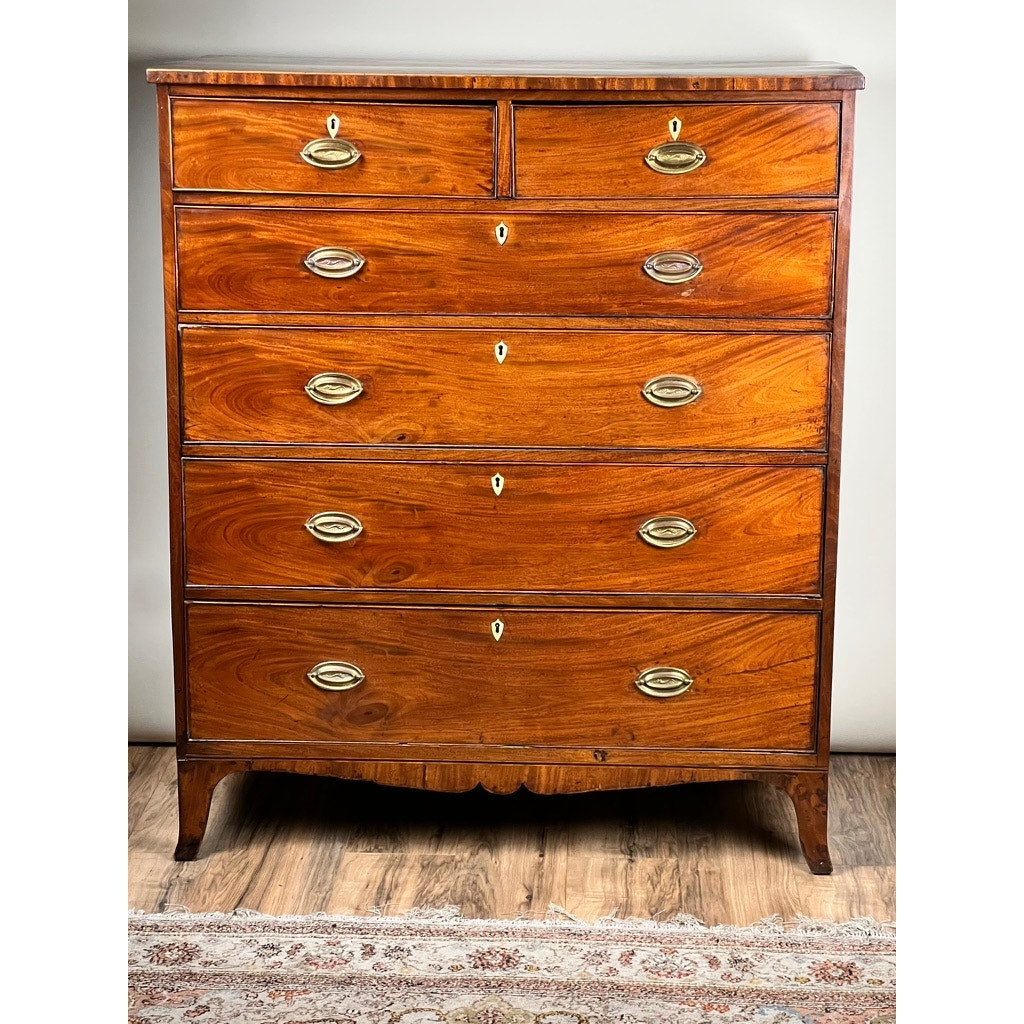 An Antique George III Two Over Four Chest with French Feet c. Early 19th Century stands on a wood floor by a patterned rug, featuring six drawers with brass handles, keyholes, and gently curved feet. Brand: None/Unknown.