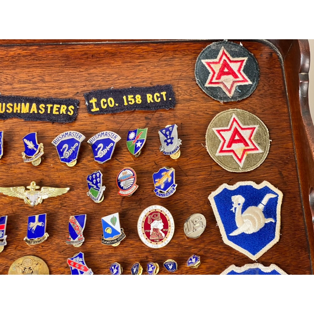 A WWII 158th Infantry Bushmasters memorabilia collection attributed to Frank W. Slatcher, Company I, Pacific Theater, featuring patches, pins, eagle wings, and emblems in blue, red, and gold—honoring a proud veteran legacy.