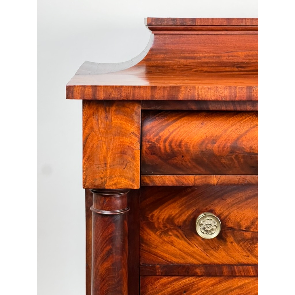 Close-up of an Antique American Empire Albany Four Drawer Chest c. 1840 in polished flame mahogany, featuring a curved top edge, visible wood grain, round brass pulls, and decorative side columns against a plain white background.