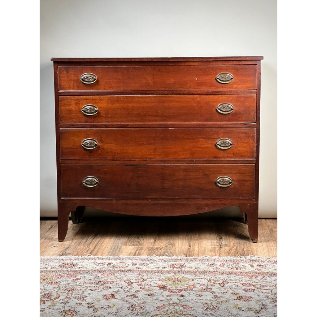 A Rare Labeled William Lloyd Springfield, Massachusetts Federal Cherry Chest of Drawers, Circa 1800, features four drawers with brass oval handles, curved front legs, and a reddish-brown finish. Standing on a wooden floor with a patterned rug in front, this classic piece echoes New England Federal furniture and showcases the refined craftsmanship associated with cabinetmaker William Lloyd.