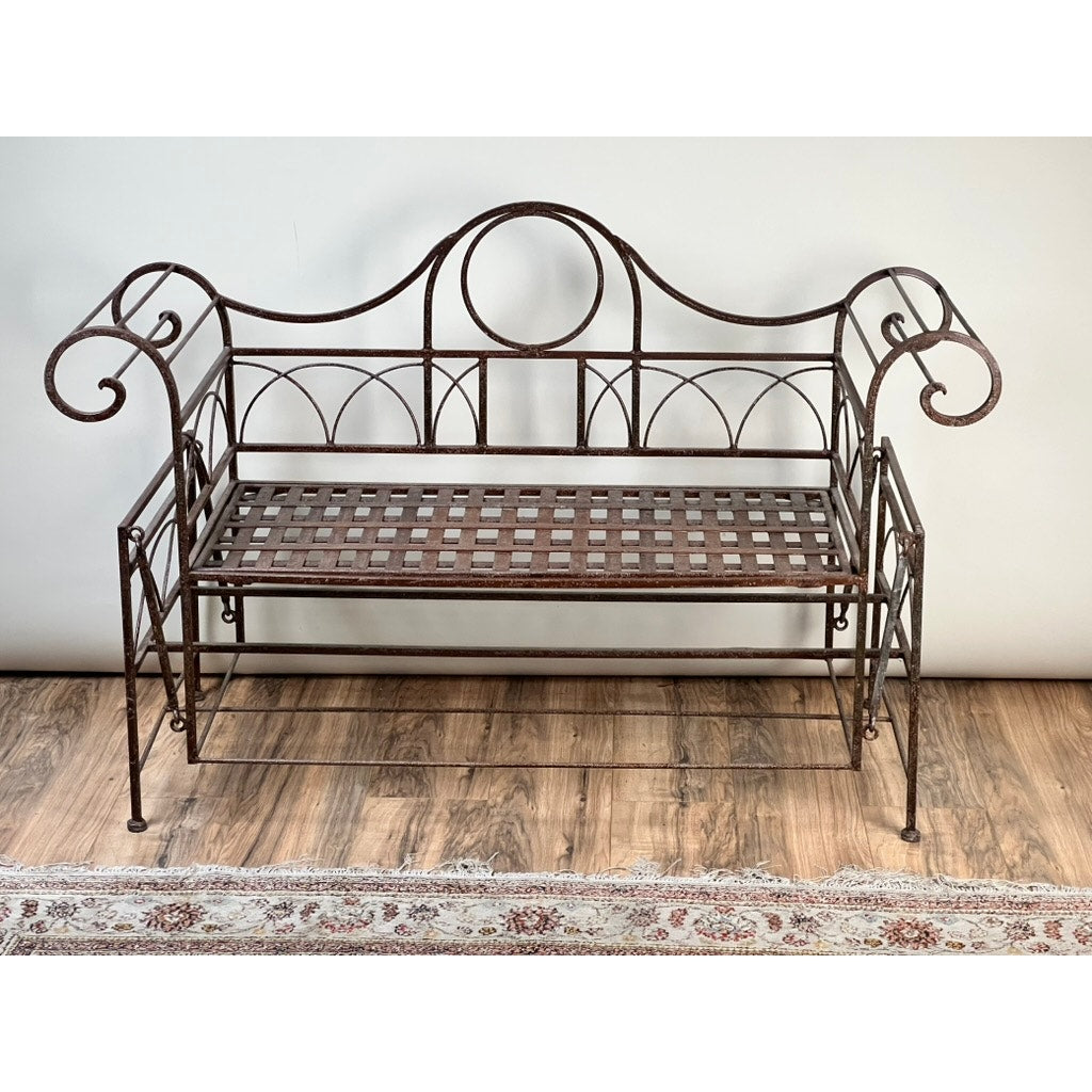 A Vintage Regency Style Wrought Iron Porch Glider with a lattice seat, curved armrests, and Regency-inspired backrest sits on a wooden floor next to a patterned rug. Brand is unknown.