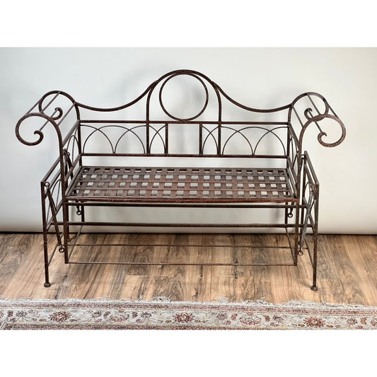 A Vintage Regency Style Wrought Iron Porch Glider by Pearl City Antiques, featuring a lattice seat and curved armrests, sits on a wooden floor near a fringed rug, set against a plain light-colored wall.