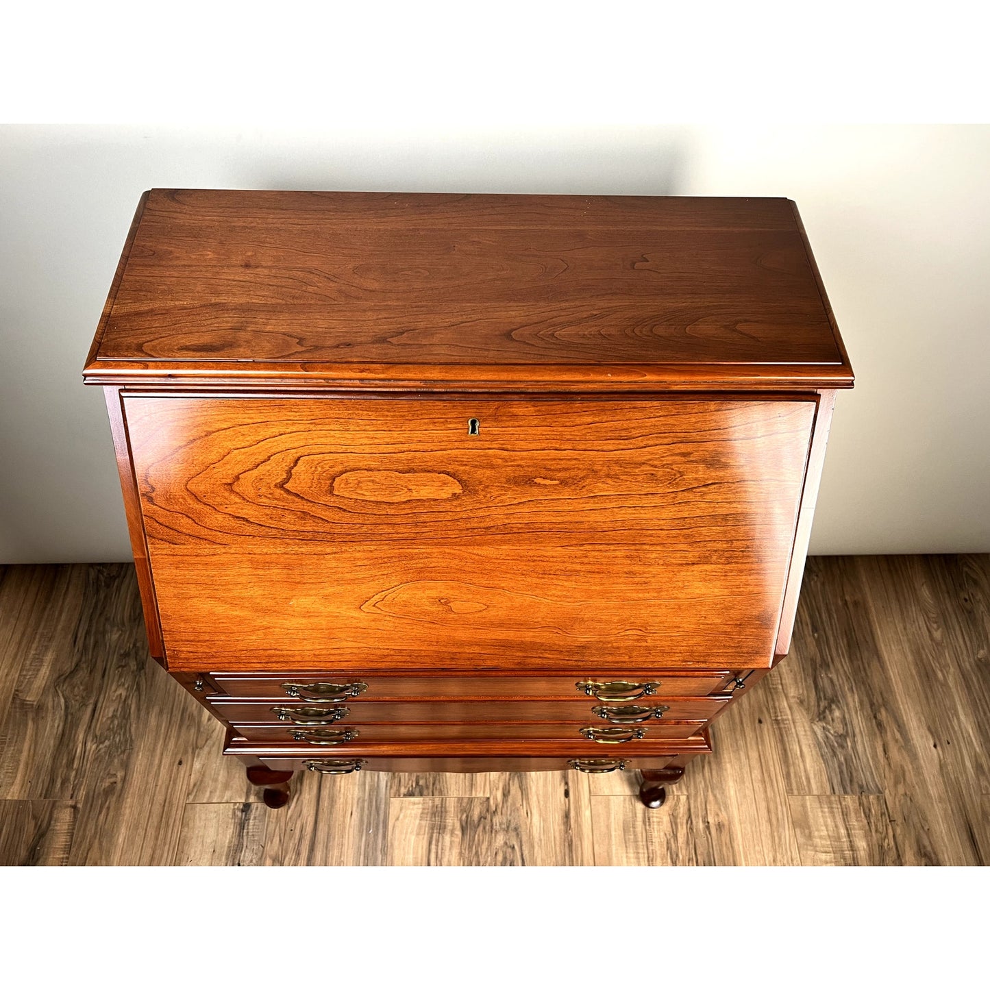 The Pennsylvania House Vintage Solid Cherry Queen Anne Style Slant Front Secretary Desk features a closed drop-front panel, multiple drawers, traditional brass handles, and a polished finish. Shown from above on a wood floor.