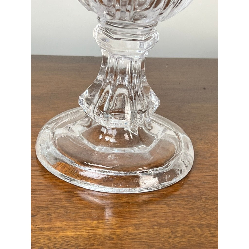 A close-up of the clear glass base and lower stem of an Antique Sandwich Glass Gothic Arch Pressed Glass Celery Vase (Boston & Sandwich Glass Co., c. 1860–1880) displayed on a polished wooden surface.