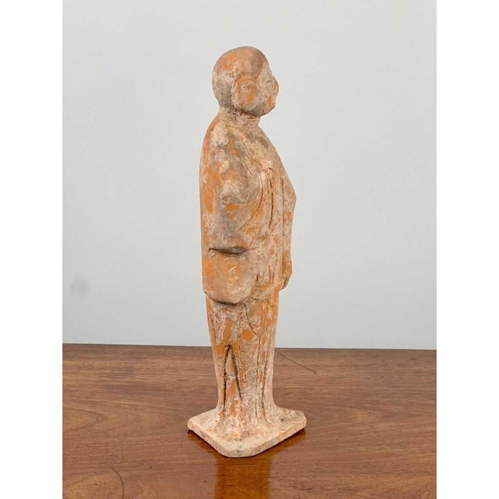 An Antique Chinese Tang Dynasty (618-907 AD) terracotta figure of a standing court lady with COA, in weathered orange and gray clay, is showcased in profile on a wooden surface against a plain light background.