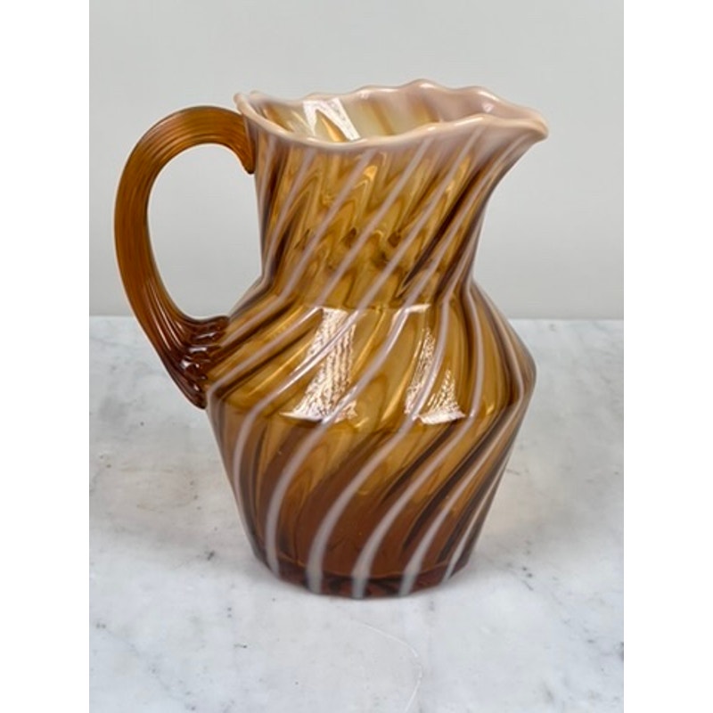 A Vintage Fenton Autumn Gold Opalescent Glass Spiral Pattern Pitcher with a wavy rim and curved handle sits on a white marble surface—a striking collectible with swirling marbled hues. Brand: Unknown.