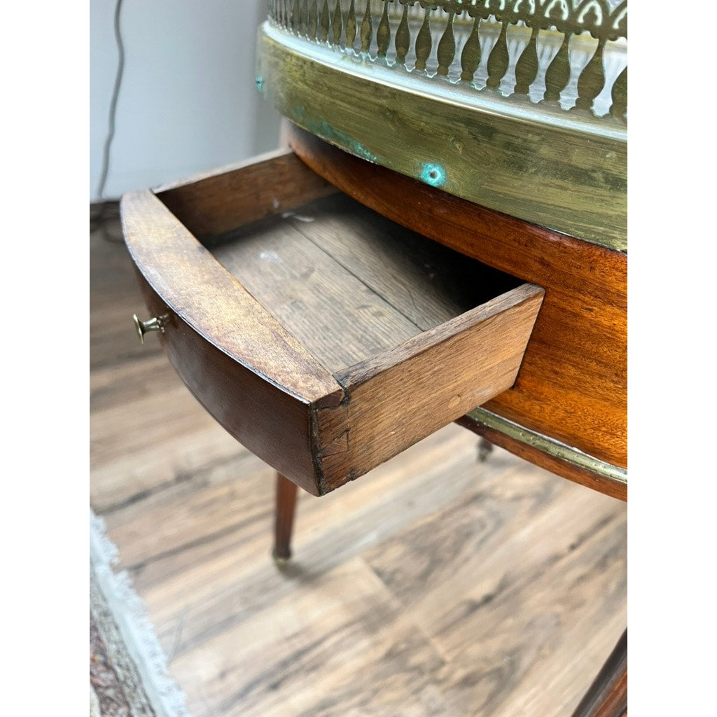 A close-up of a small mahogany drawer partially open in an antique 19th century French Louis XVI-style bouillotte table with marble top and pierced brass gallery, standing on a wooden floor beside a rug.