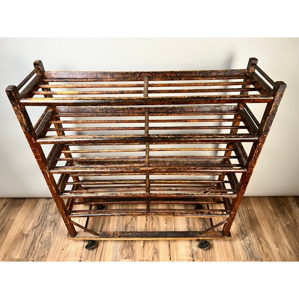 An Antique Oak Shoe Factory Rolling Rack on original industrial casters (late 19th century) stands on a wooden floor against a light wall, featuring brown oak and multiple horizontal slats. Brand: None/Unknown.