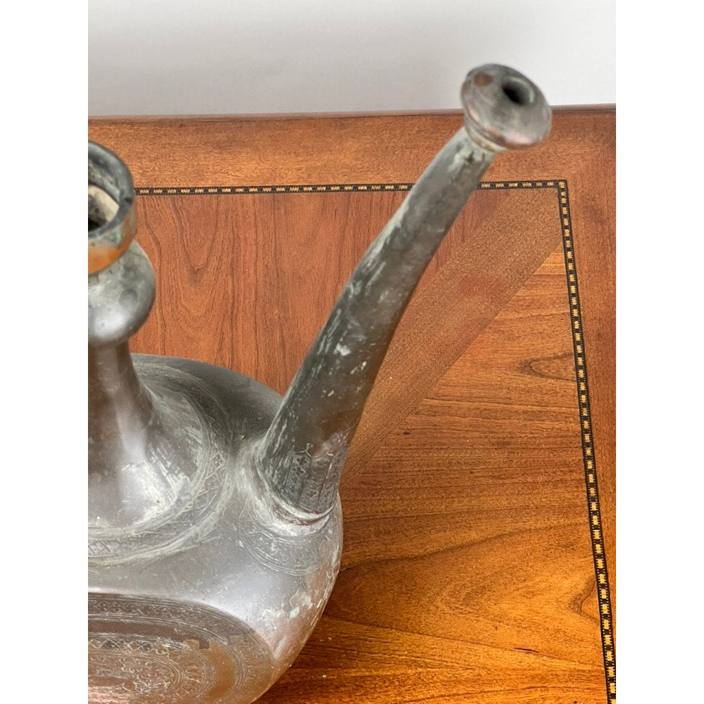 A close-up of an Antique Qajar Persian Copper Engraved Ewer (19th Century), featuring fine Persian metalwork, displayed on a polished wooden table with an inlaid border. Brand: Unknown.