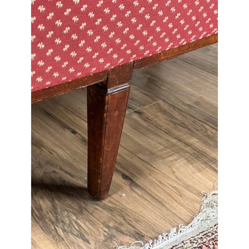 Close-up of a wooden leg on a piece of furniture with a red patterned fabric background.