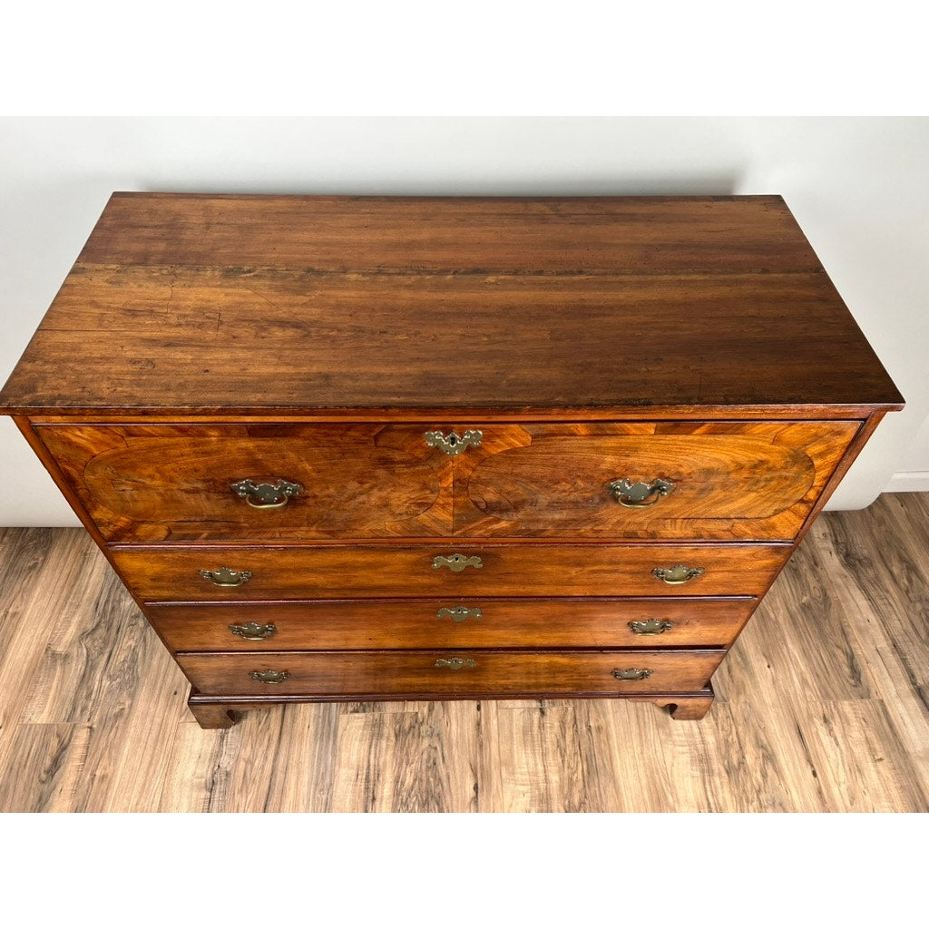 An Antique George IV Butlers Secretary from the early 19th century, featuring four drawers with ornate brass handles and a rich brown wood grain, stands on a light wood floor against a plain white wall. Brand: None/Unknown.