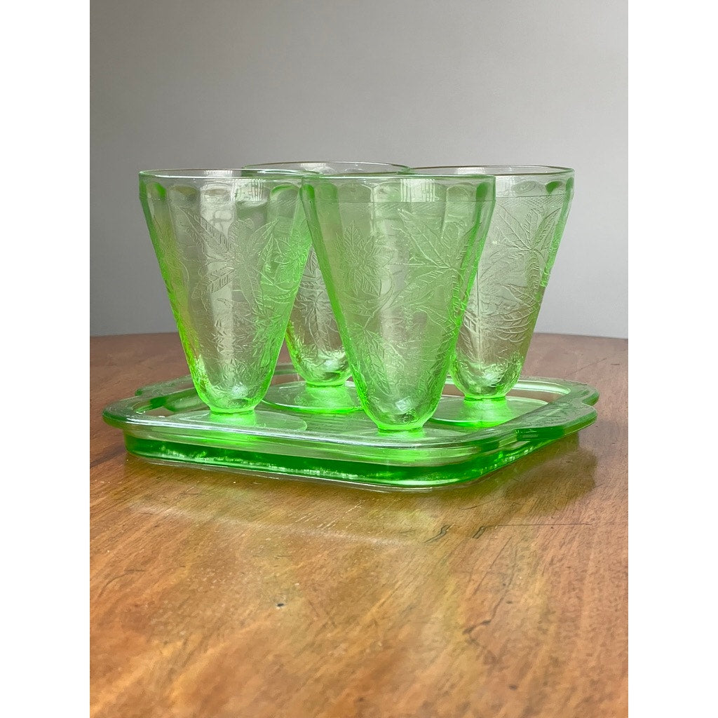 Antique Jeannette Glass Co. Green Uranium Floral Poinsettia 5-piece beverage set (c. 1930s) with four cups and a matching tray is displayed on a wooden surface against a plain light background.
