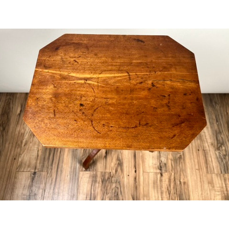 An Antique 19th Century Cut Corner Hepplewhite Candle Stand with visible scratches and marks sits on a wooden floor near a plain white wall.