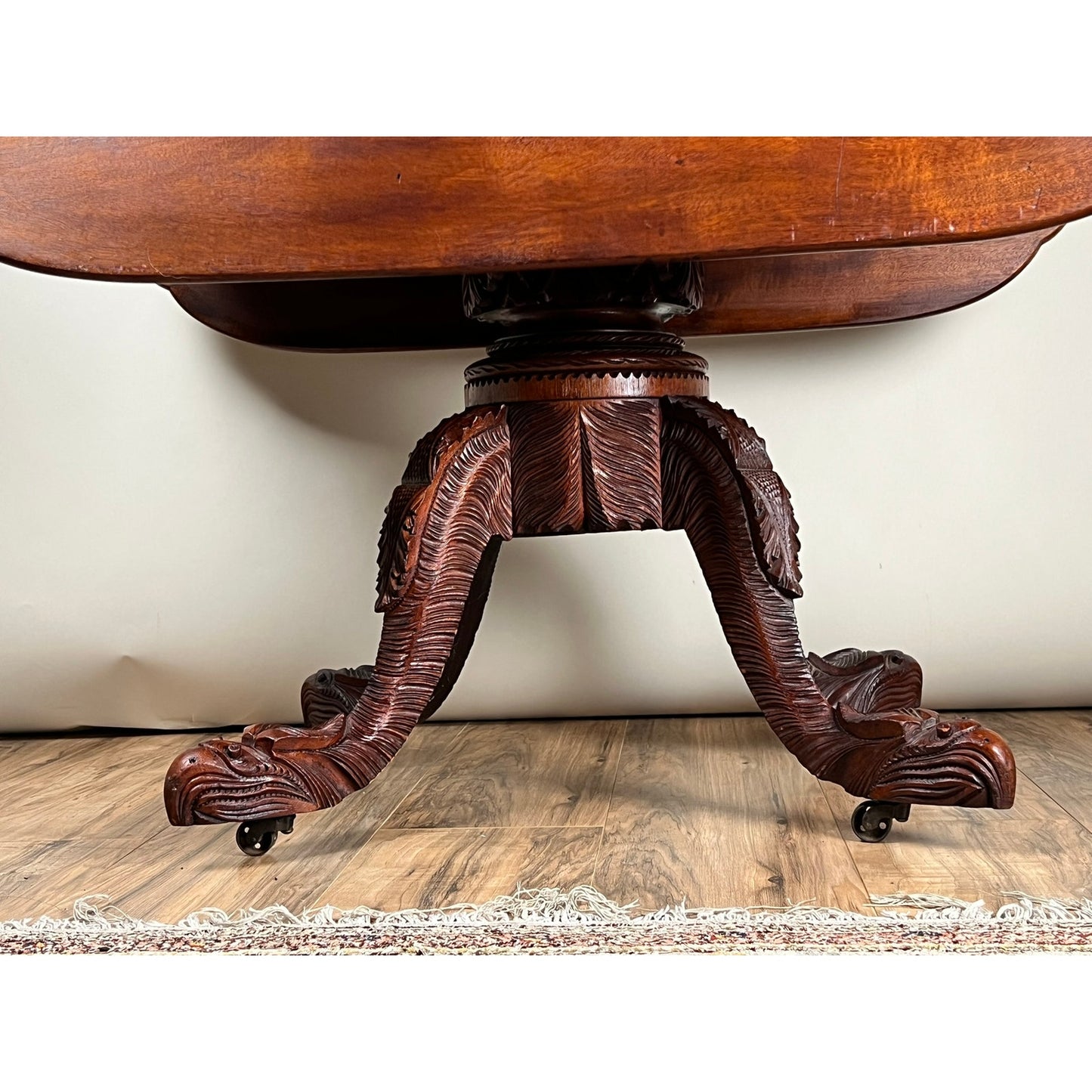 A close-up of the Antique American Empire Drop Leaf Table c. 1840 shows its intricately carved eagle feet on casters, set on a wooden floor with part of a decorative rug visible at the bottom.