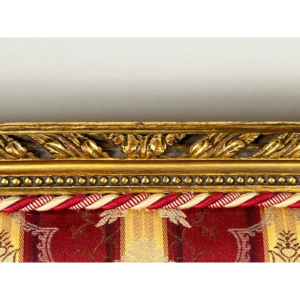 Close-up of an Antique Louis XVI Style Giltwood Settee in Silk Damask, late 19th century, showing its ornate carved gold frame above rich red and gold striped silk fabric with decorative cord trim. Brand: Unknown.
