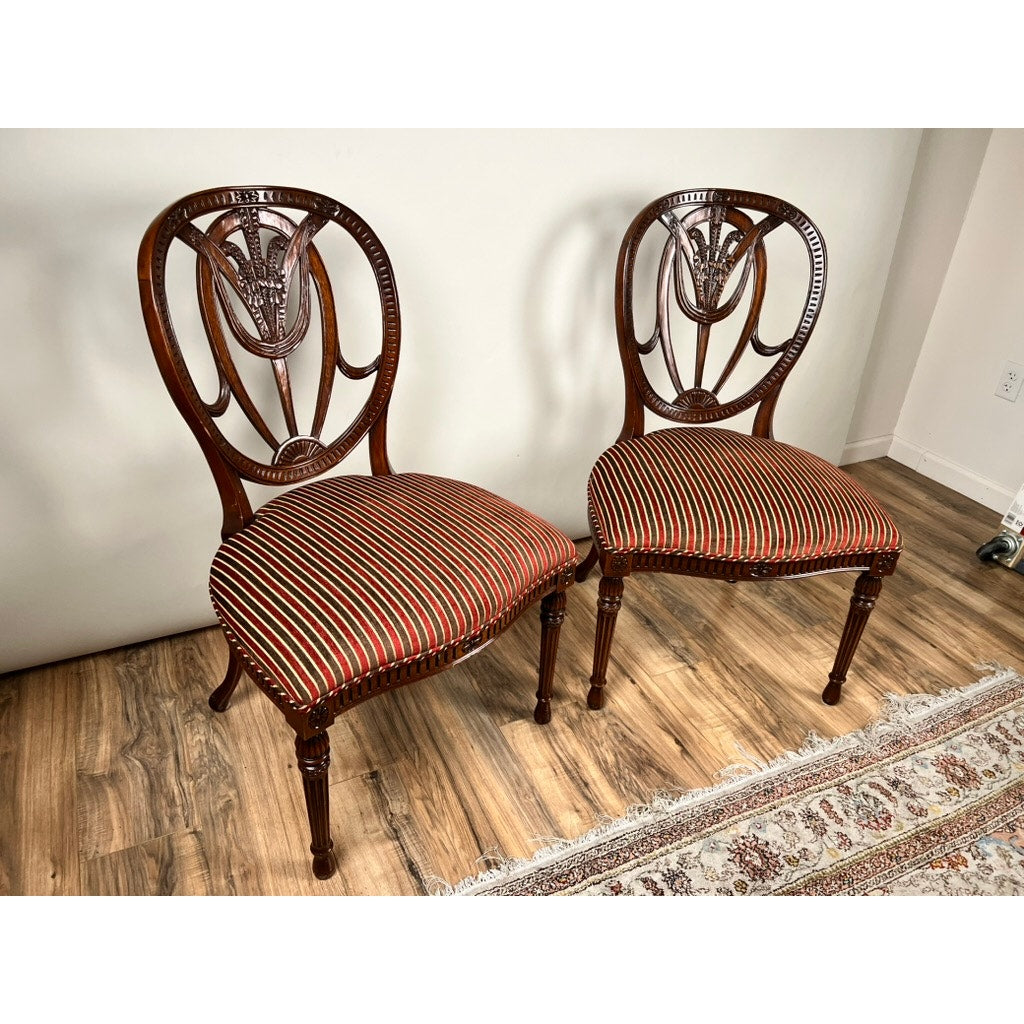 A vintage pair of Ardley Hall Wheel Back Side Chairs by Ardley Hall features carved backs and striped upholstery in red, black, and gold, positioned on a wood floor next to a patterned rug against a plain white wall.
