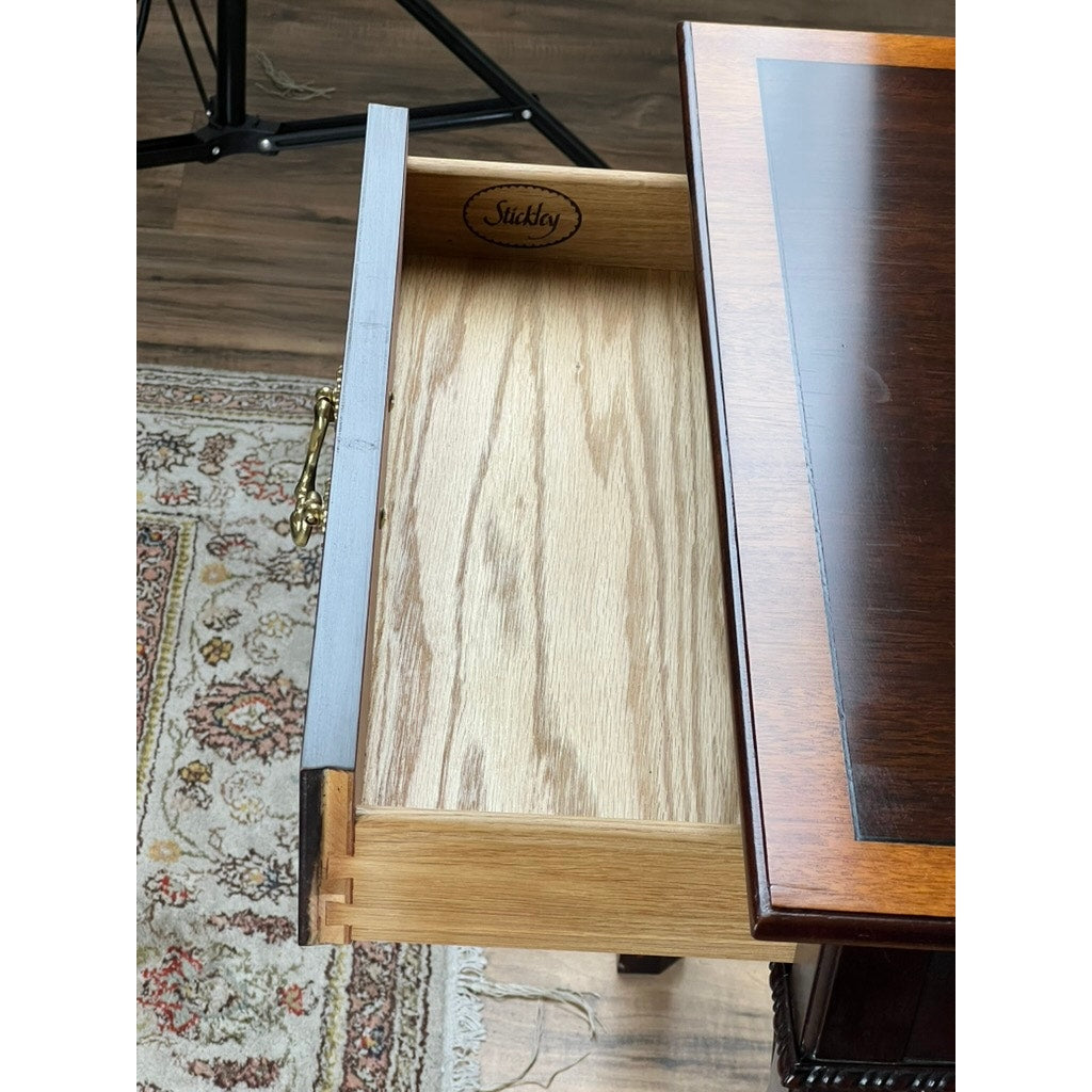A Vintage Federal Style X Stretcher One Drawer End Table by Stickley, featuring dovetail joints and a branded interior, is shown attached to a dark wood desk beside a patterned rug on a wooden floor.