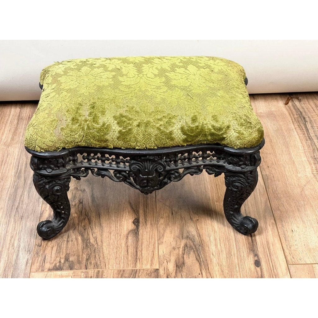 An Antique Victorian Cast Iron Foot Stool c. 1900, featuring a green patterned cushion and decorative trim, is the perfect accent furniture for any room and looks beautiful displayed on a wooden floor. Brand: Unknown.