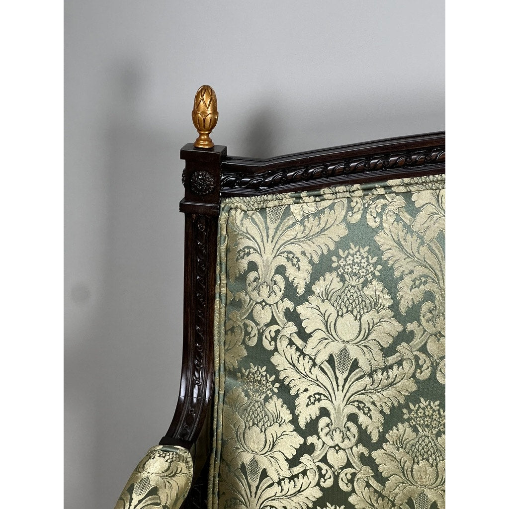 A close-up of a Vintage Louis XVI Style Settee in green damask upholstery, featuring an ornate dark carved wooden frame, gold finial on top, and intricate floral patterns. Brand: Unknown.