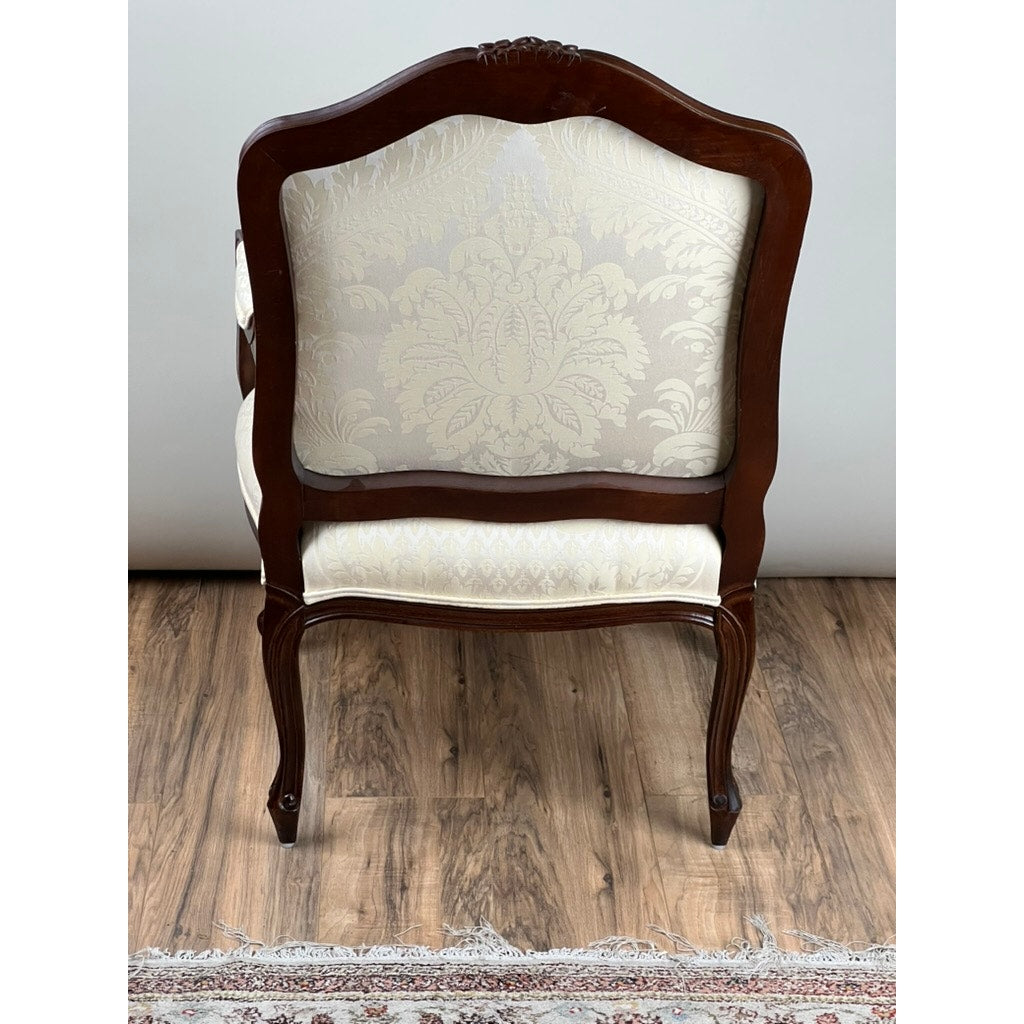 A Vintage Louis XV Style Fauteuil Arm Chair by Pennsylvania House, featuring a wooden frame and cream floral upholstery, sits on a hardwood floor. Shown from the back, a fringed rug is partially visible at the bottom of the image.