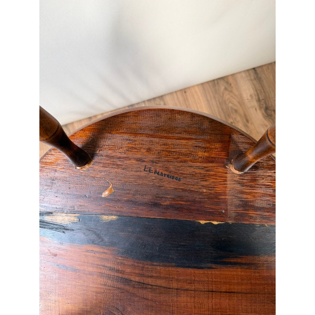 The underside of a wooden chair seat with two legs visible and L.E. Partridge Connecticut stamped on the wood. The seat displays signs of wear and natural wood grain with variations in tone, highlighting the lasting craftsmanship characteristic of bench-made Windsor chairs from the 1960s.