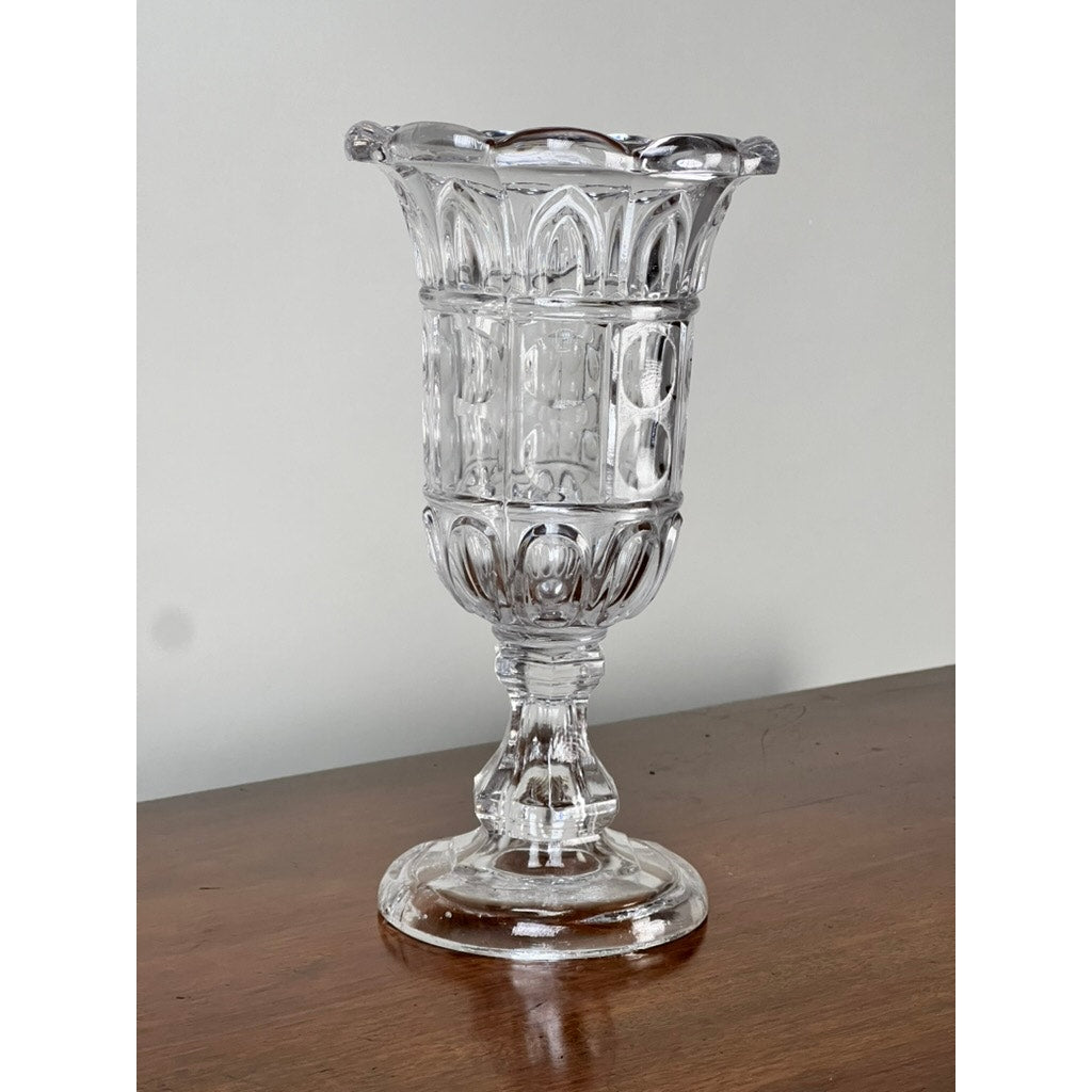 An Antique Boston & Sandwich Glass Co. Gothic Arch Pressed Glass Celery Vase (c. 1860–1880) by Sandwich Glass features a flared, scalloped rim, intricate geometric designs, and stands on a short pedestal base—showcasing classic craftsmanship.