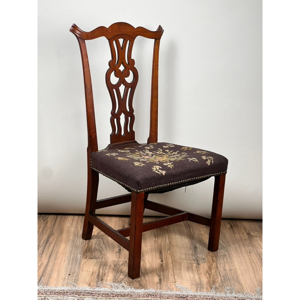 An Antique Chippendale Side Chair with a decorative carved backrest and a needlepoint seat (mid-19th century, brand unknown) sits on a wood floor against a plain light background.