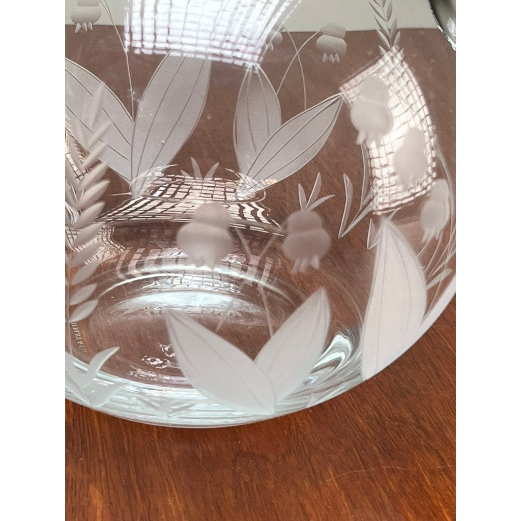 A Vintage Tiffany & Co. etched crystal pitcher featuring a delicate lily of the valley floral motif sits on a wooden surface, reflecting a window grid across its branded surface.