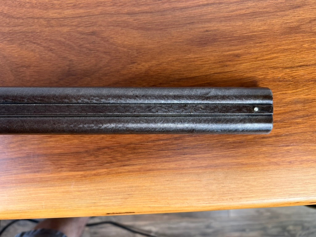 Close-up of a dark, cylindrical metal component featuring a groove and a small bolt, resting on a reddish-brown wooden surface—likely part of the Antique Christoph Funke Suhl German Damascus Double Barrel Hammer Shotgun with carved stock, c. 1880, offered by Pearl City Antiques.
