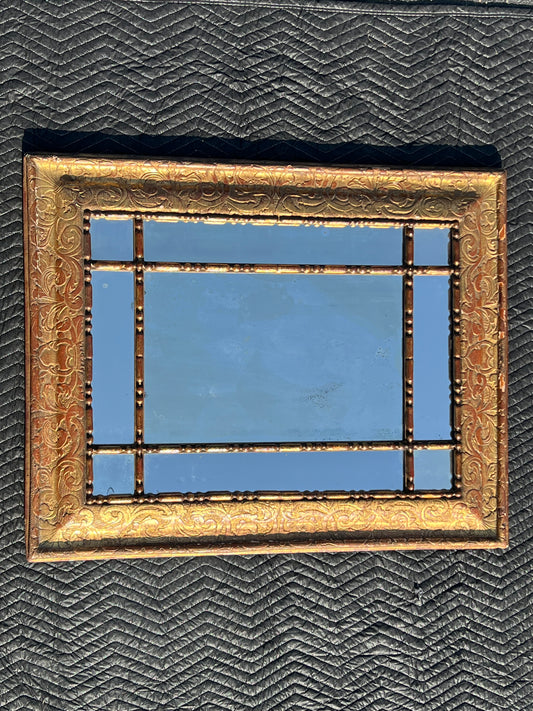The Pearl City Antiques Antique 18th Century Italian Baroque Gilt Wood Mirror 35 x 43, with an ornate gold frame and decorative grid, is mounted on a dark, zigzag-patterned background reflecting the blue sky.