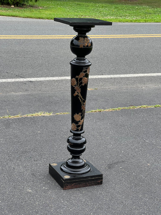 A Vintage Ebonized Aesthetic Movement Style Pedestal with Brass Applique by Pearl City Antiques stands on asphalt near a road with yellow dividing lines and green grass in the background.