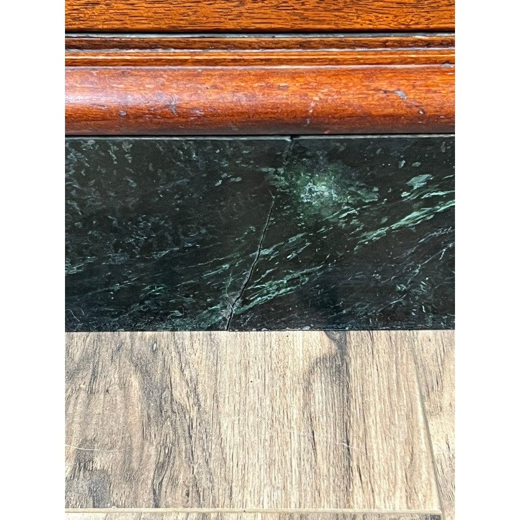 Close-up showing the Antique Mahogany Multi-drawer Dental Cabinet by The American Cabinet Co. (early 20th c.) on top, dark green marble with pale veining in the middle, and light brown wood-patterned flooring at the bottom.