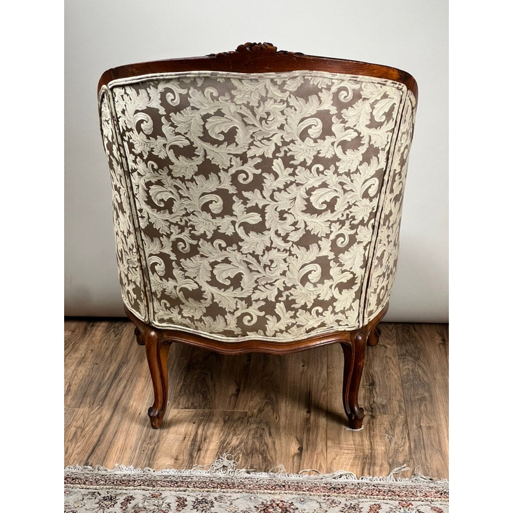 An Antique French Louis XV Rococo Style Bergère Arm Chair, c. Mid 19th Century, with a carved walnut frame and newer damask upholstery is shown from the back, set on a wooden floor near a patterned rug. Brand: None/Unknown.