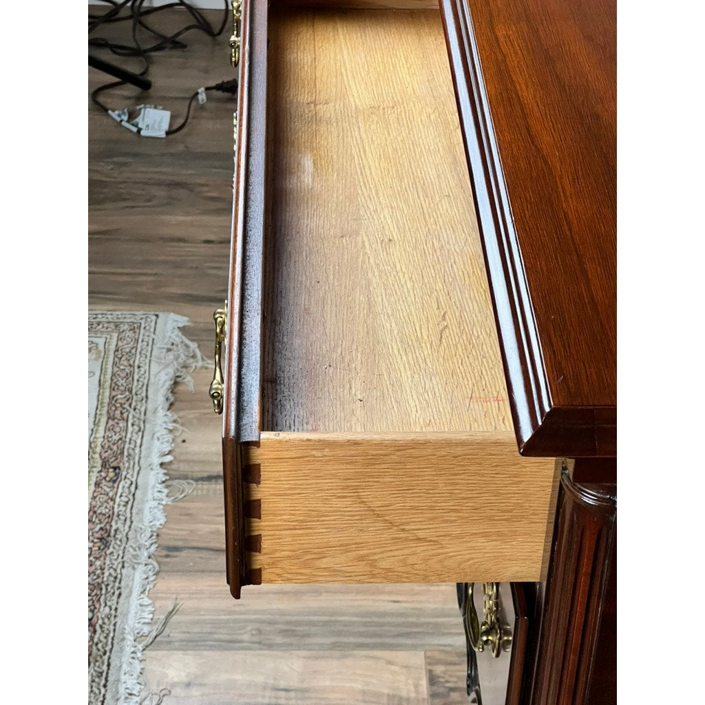 A close-up of an open drawer in a polished Councill Craftsmen Vintage Solid Mahogany Chippendale Style Lowboy shows dovetail joints, ornate brass handles, and sits on a wooden floor near a fringed rug with cords visible in the background.