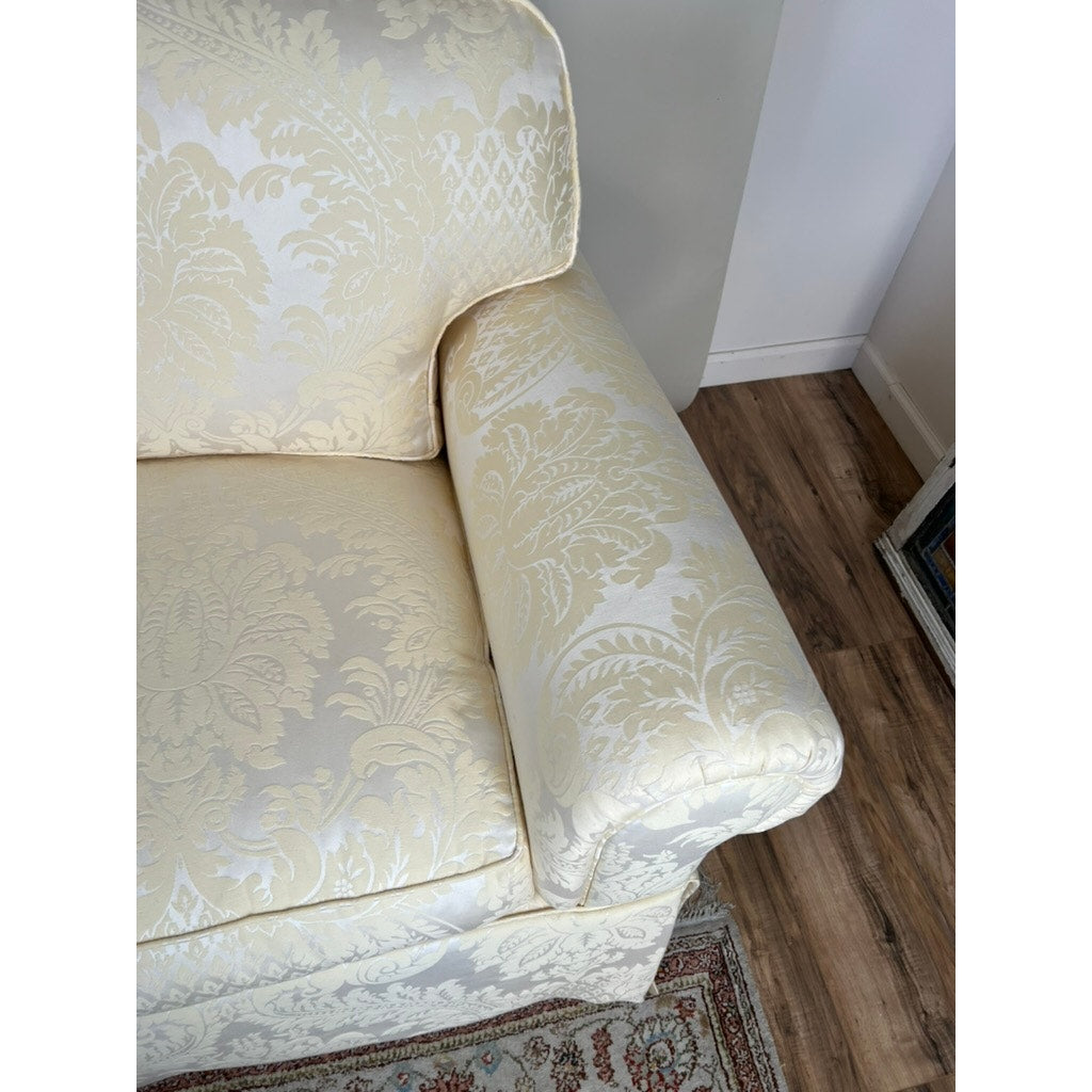 A close-up of the Vintage Custom Ivory Upholstered Sofa by Stickley, showcasing its subtle floral damask pattern, placed on a patterned rug over a wooden floor near a white wall.