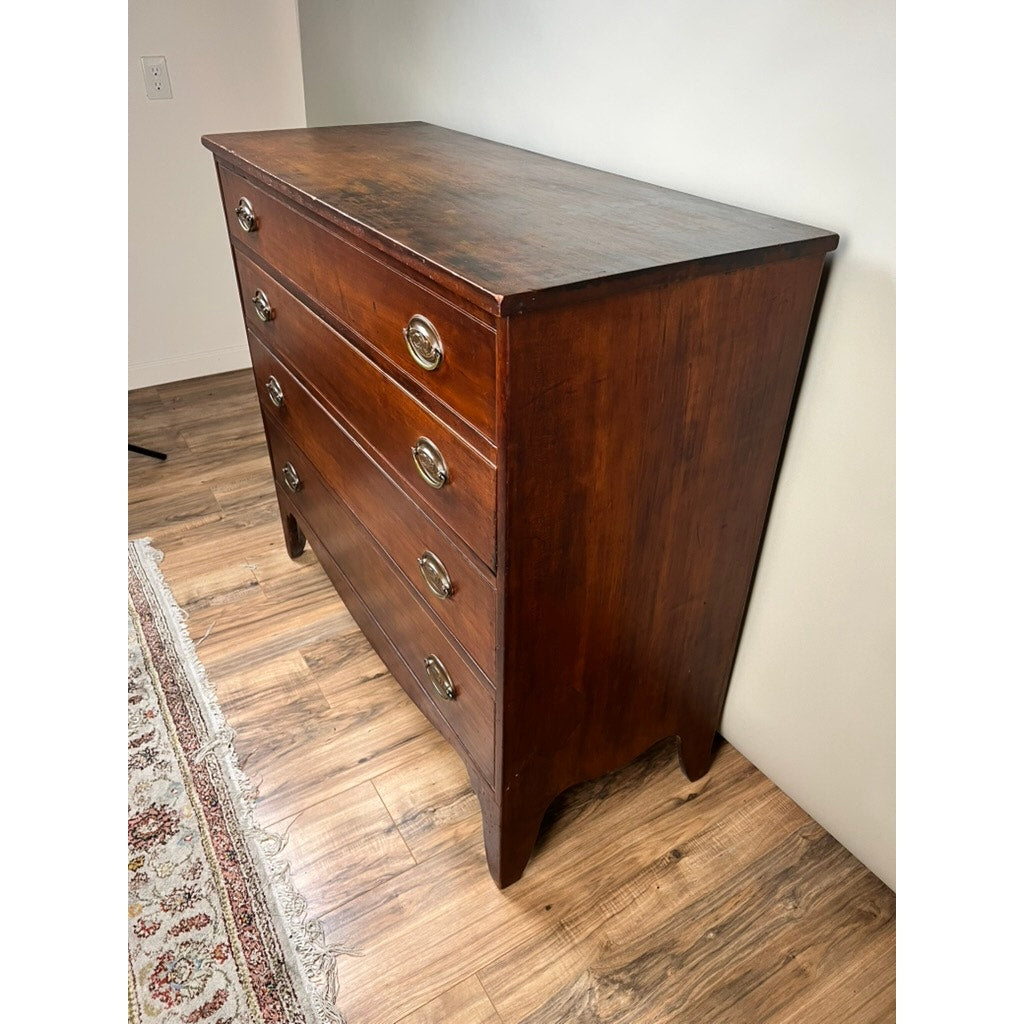 A rare labeled William Lloyd Springfield, Massachusetts Federal cherry chest of drawers, circa 1800, inspired by New England Federal period craftsmanship, features four drawers with round metal handles. The chest is elegantly positioned on a wood floor beside a patterned rug and set against a light-colored wall.