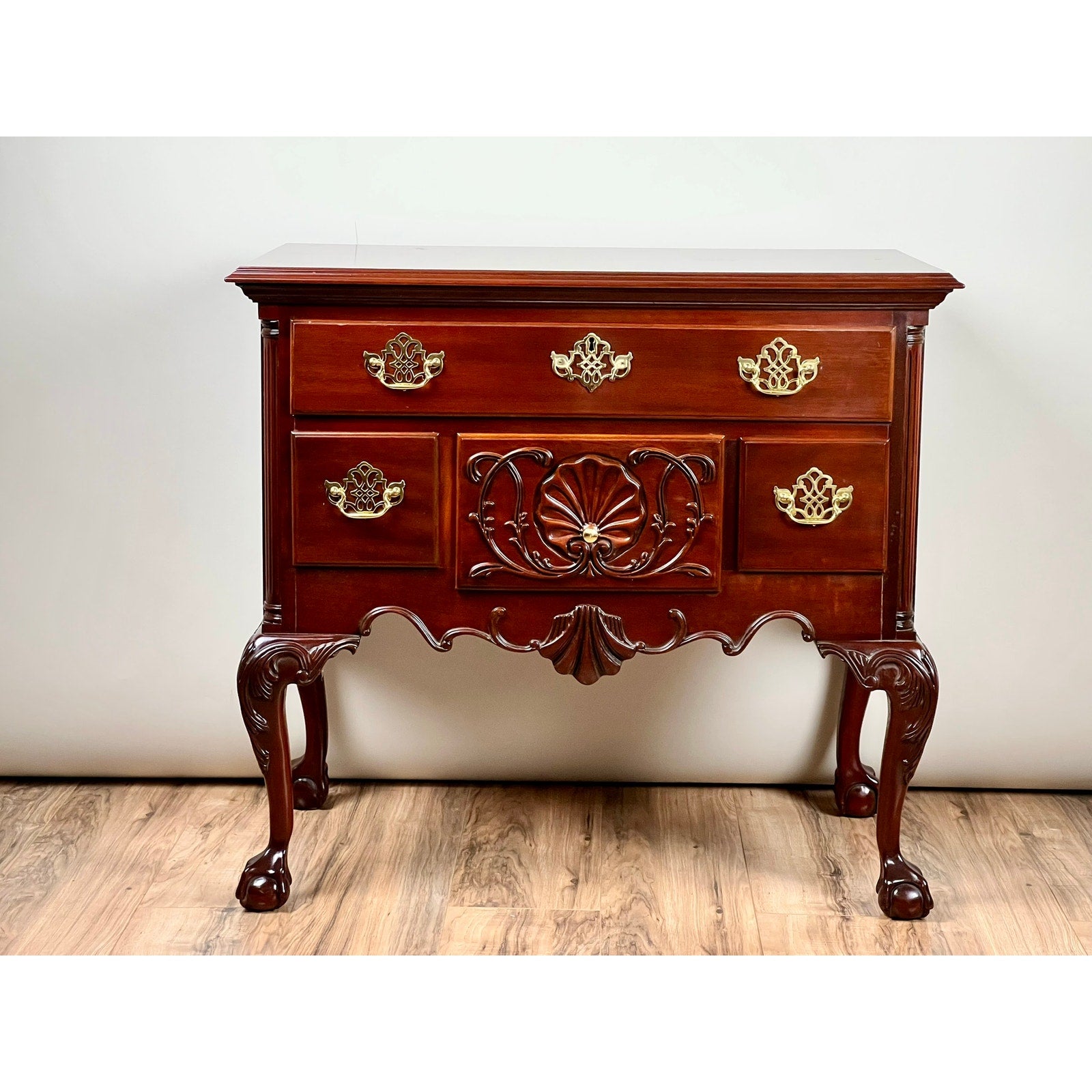 A Vintage Solid Mahogany Chippendale Style Lowboy by Councill Craftsmen, featuring ornate carvings, gold handles, three upper drawers, two larger lower drawers, and claw-foot curved legs, stands against a plain wall on a wood floor.