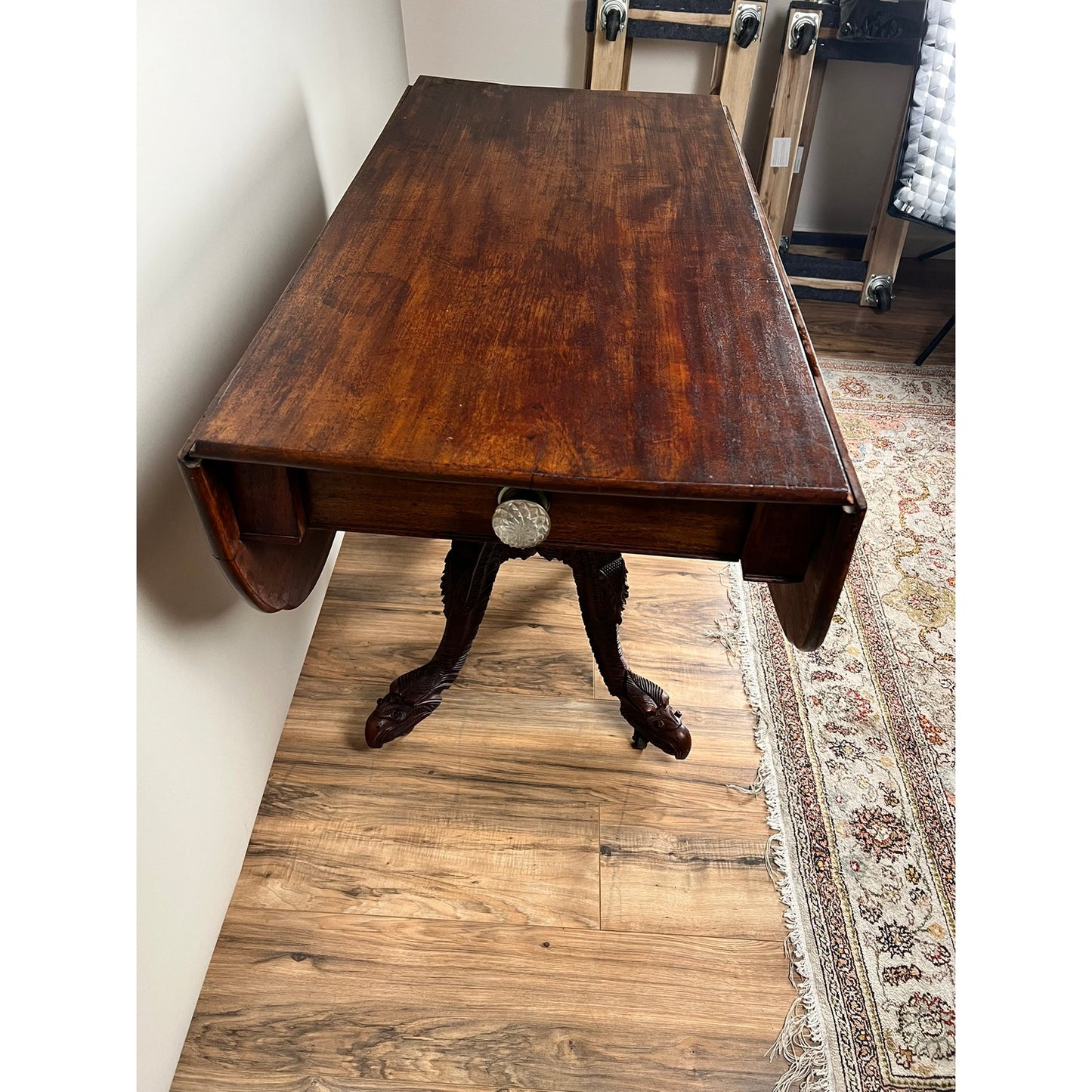 An Antique American Empire Drop Leaf Table with Great Eagle Carved Feet c. 1840 sits near a wall on a wood floor, beside a patterned rug. Brand: Unknown.