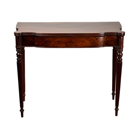 The Antique Federal Period Sheraton Cookie Corner Game Table c. 1830 features a rich mahogany finish, a curved front edge, and four slender ornate legs, capturing the elegance of Federal era furniture against a white background.