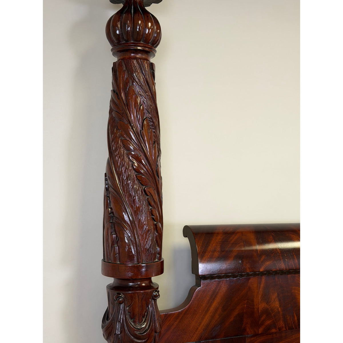 A close-up of an American Classical Carved Mahogany Four-Poster Tester Bed, Possibly New York, circa 1825–1840, showing a detailed acanthus leaf design carved into the post next to the headboard.