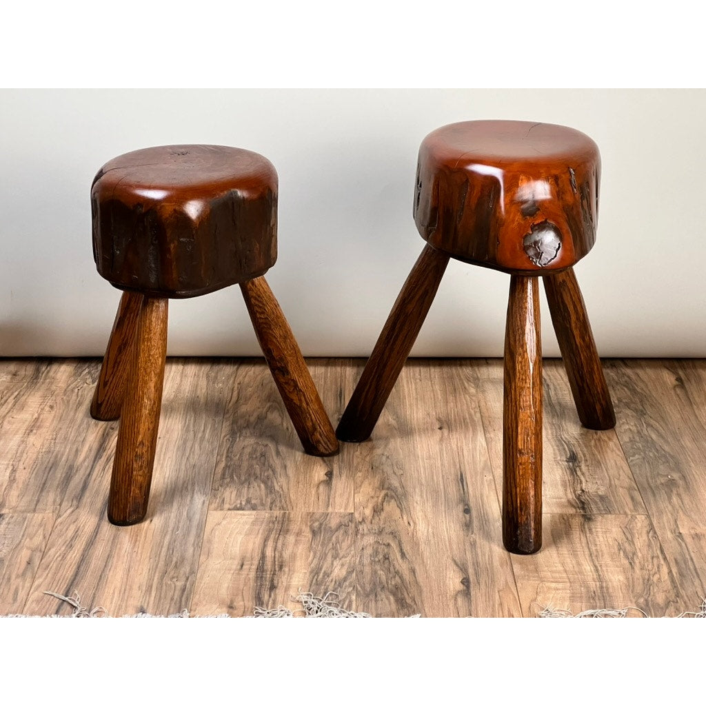 A Pair of Vintage Live Edge Wabi Sabi Cherry Stools, signed by Neil Panyik, sit on a wooden floor against a white wall, highlighting their handcrafted charm and natural aesthetic.