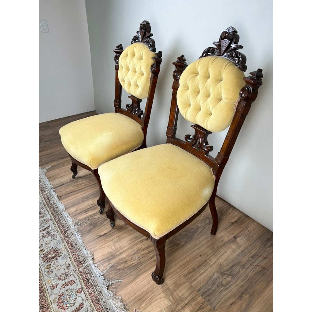 A fine antique pair of Renaissance Revival walnut side chairs, attributed to John Jelliff (Newark, c. 1880), feature intricately carved backs and legs with tufted yellow velvet upholstery, set on a wooden floor near a patterned rug.