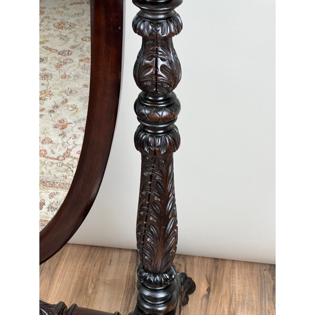 Close-up of an Impressive Antique American Empire Acanthus and Barbola Rose Carved Cheval Mirror c.1840, showing detailed dark wood leg with carved leaf patterns on a wooden floor, part of a patterned rug, and curved mirror frame in view.