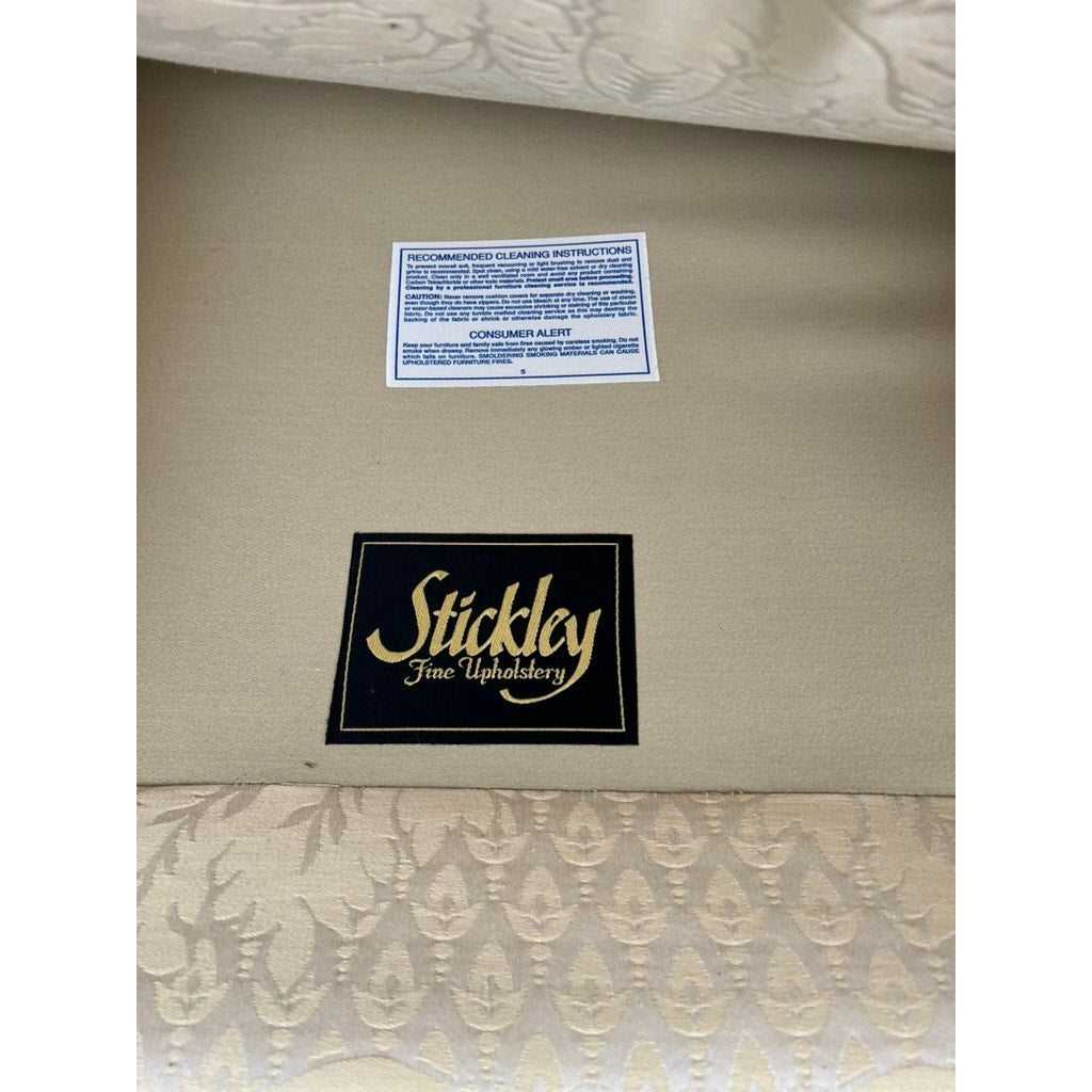 Close-up of a Vintage Custom Ivory Upholstered Sofa by Stickley, showing the black and gold “Stickley Fine Upholstery” label and blue and white cleaning tag above. Patterned fabric appears at the bottom.