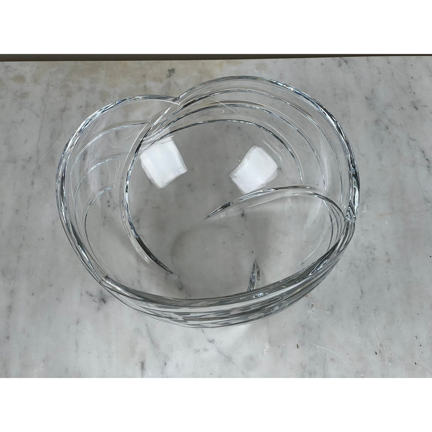 The Rogaska Samba Wave 10" Lead Crystal Bowl features a modern swirling design and overlapping glass sections, shown here on a light gray marble surface.