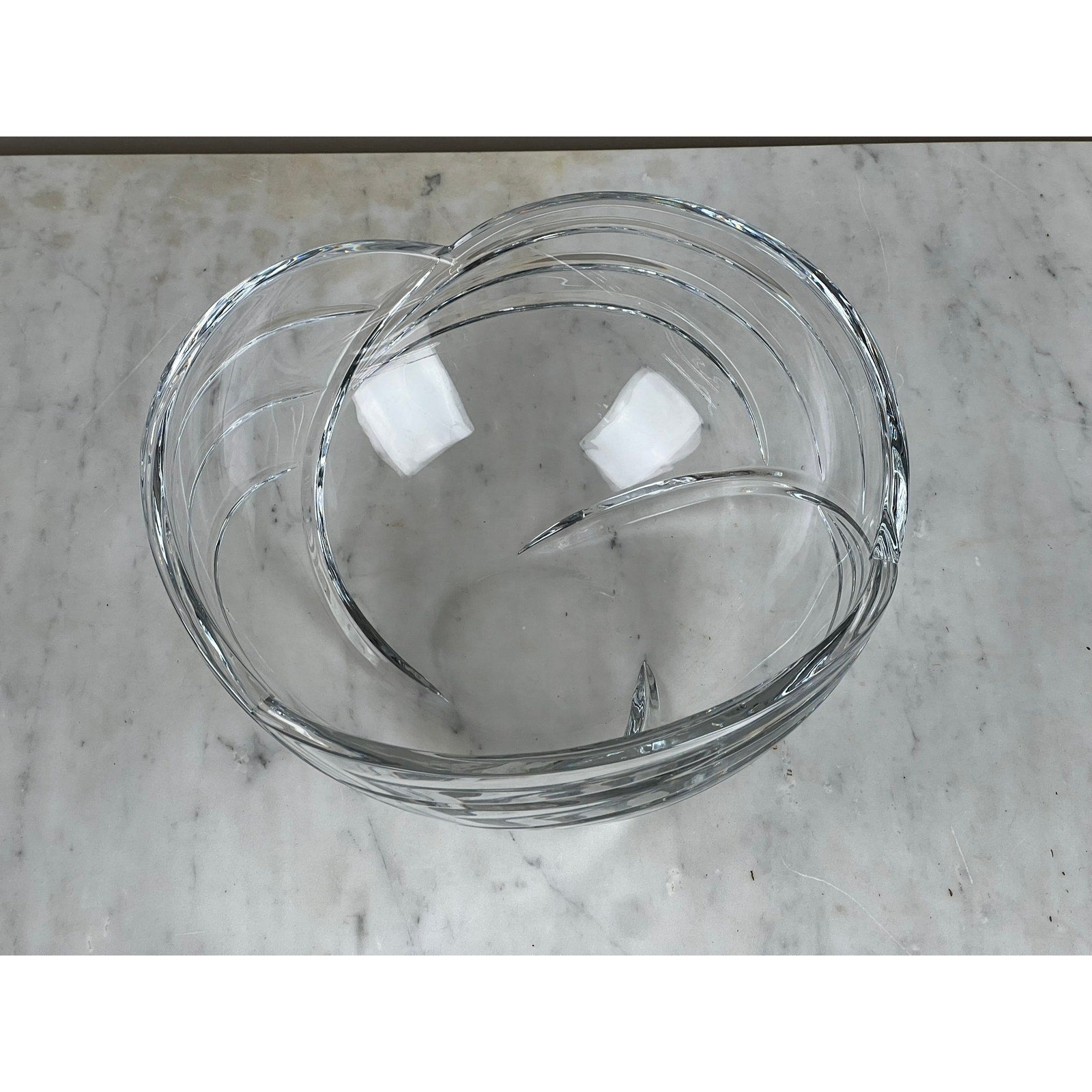 The Rogaska Samba Wave 10" Lead Crystal Bowl features a modern swirling design and overlapping glass sections, shown here on a light gray marble surface.