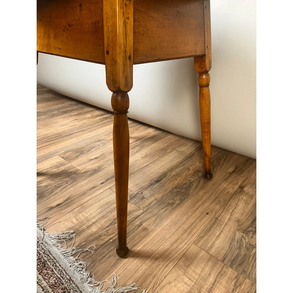 A close-up of the legs of an Antique American Queen Anne Maple Tavern Table (New England, circa 1760–1790) on a wood-patterned floor, with part of a fringed rug visible in the lower left corner.