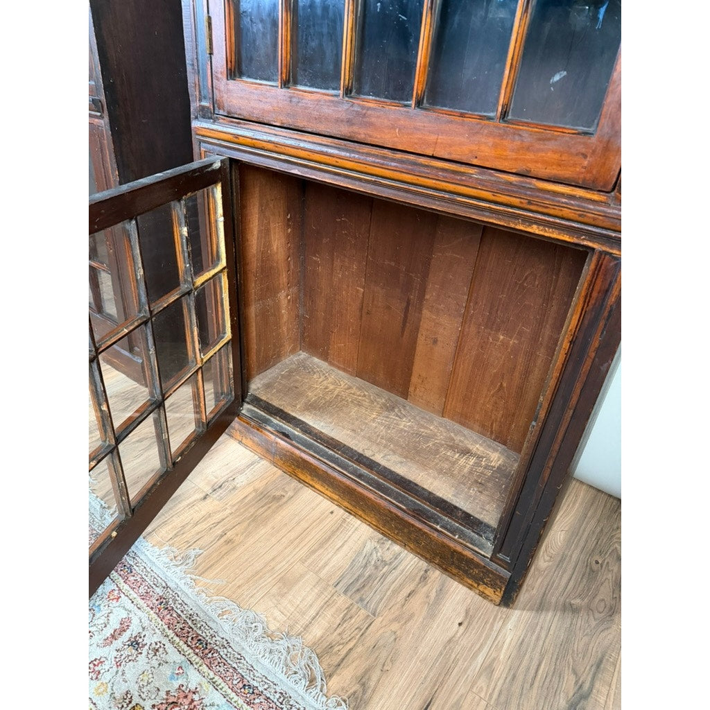 A Pair of Mid-19th Century New England Cherry Glazed Display Cupboards, c. 1840–1860 from Pearl City Antiques stands open with glass-paneled doors, revealing empty interiors and visible shelves; evocative of early American design, they are positioned on a hardwood floor beside a patterned rug.