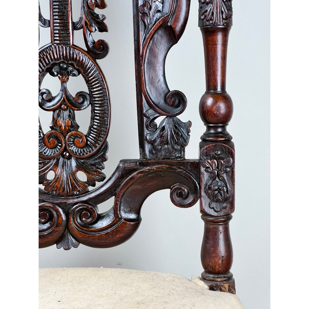 Close-up of an Antique Fine Carved Flemish Side Chair, attributed to Daniel Marot (late 17th century), showing intricate floral and scroll carvings in dark wood on the backrest and arm, with a light upholstered seat below.