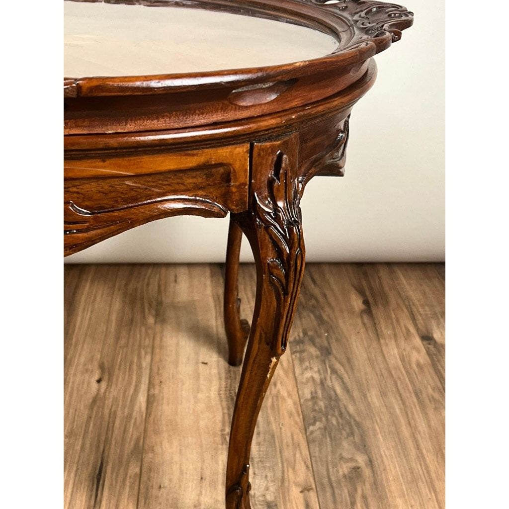 Close-up of a Vintage Louis XVI Style Butlers Table with removable glass tray, featuring carved floral details on the legs and edges, set on a wooden floor against a light-colored wall. Brand: Unknown.